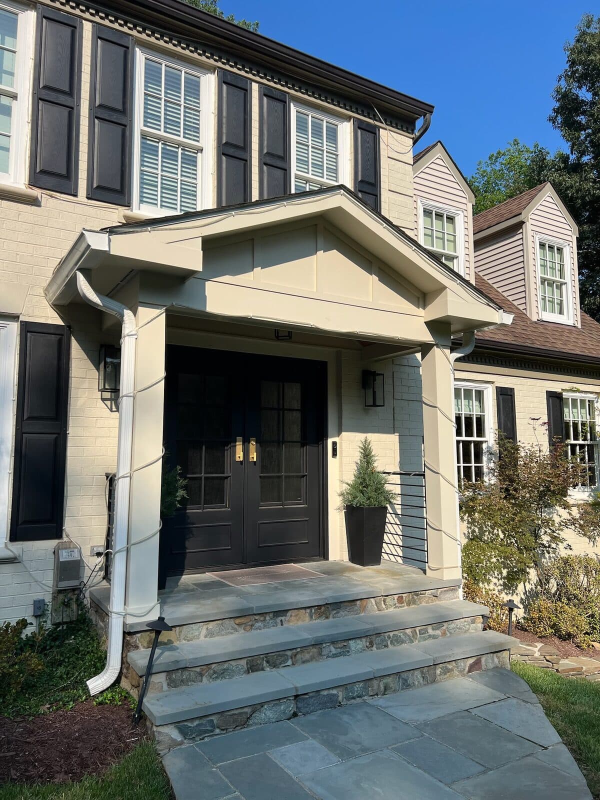 Cream colonial home with covered front porch entrance and dark double doors