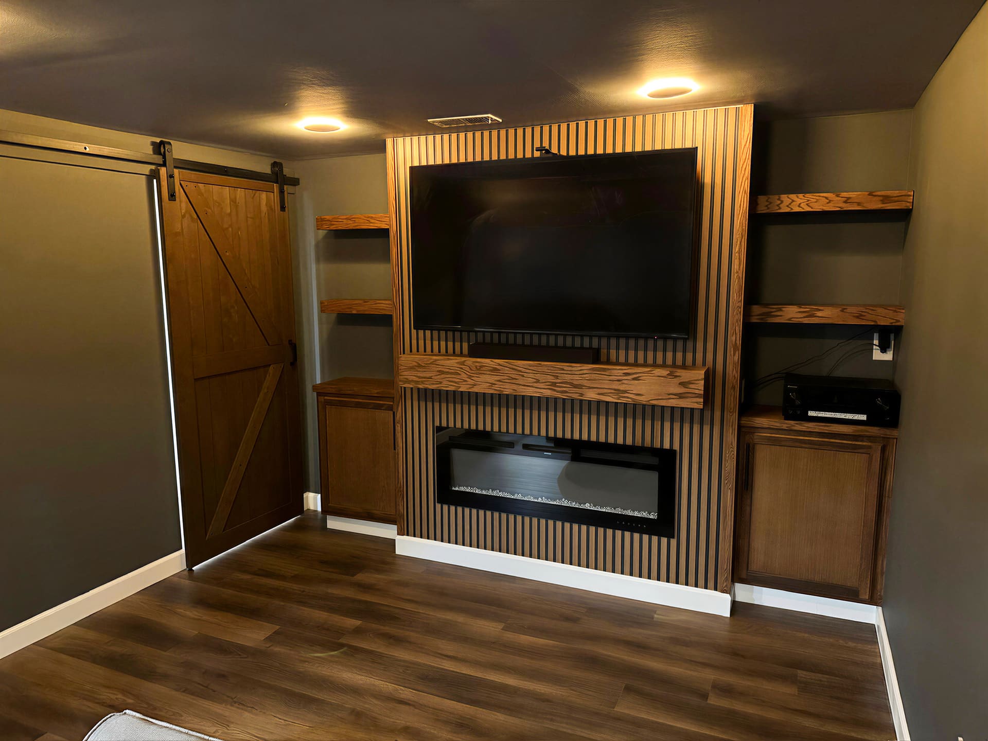 Custom wood slat media wall with built-in electric fireplace and barn door