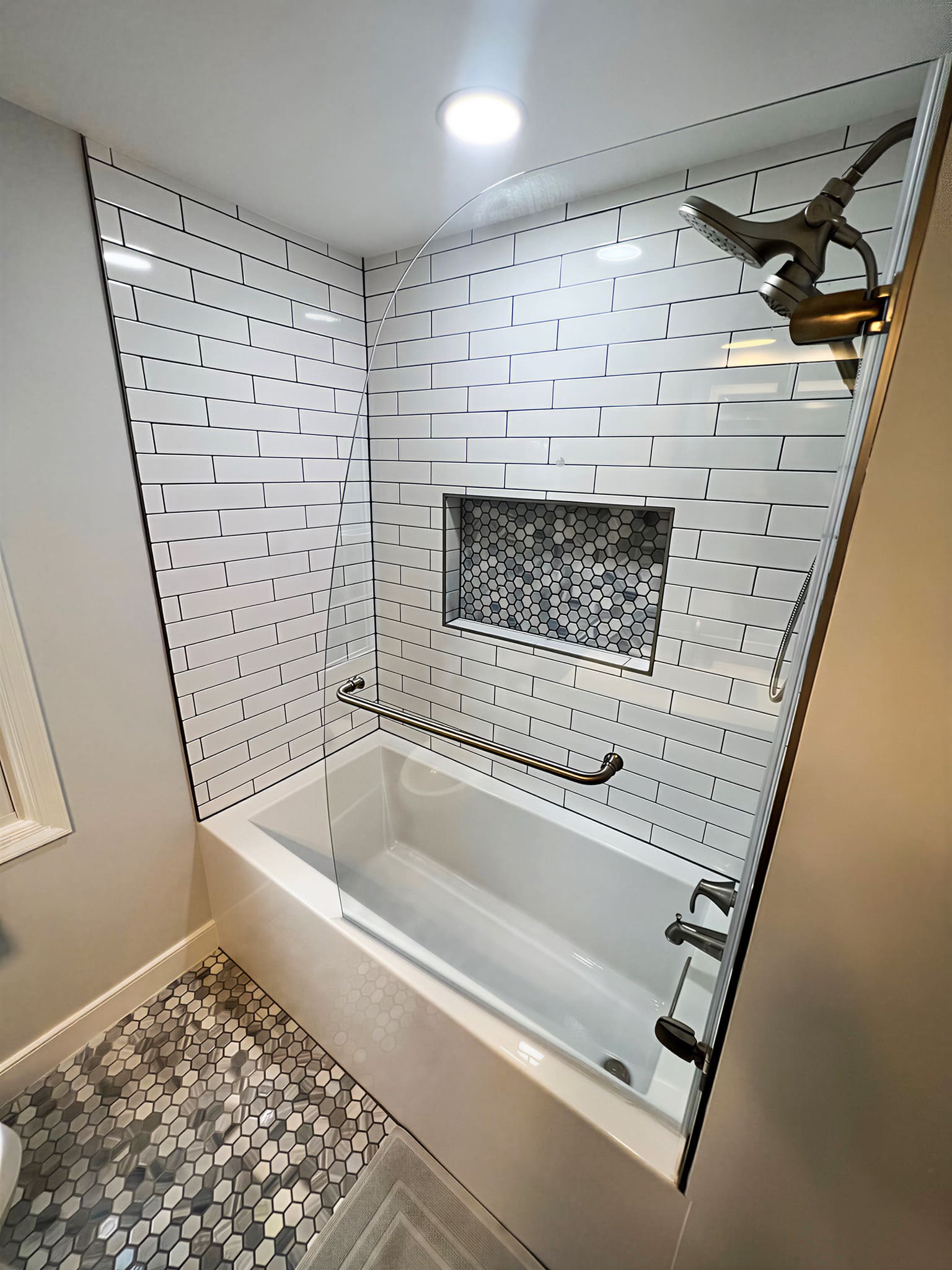 White subway tile tub and shower with hexagon mosaic niche