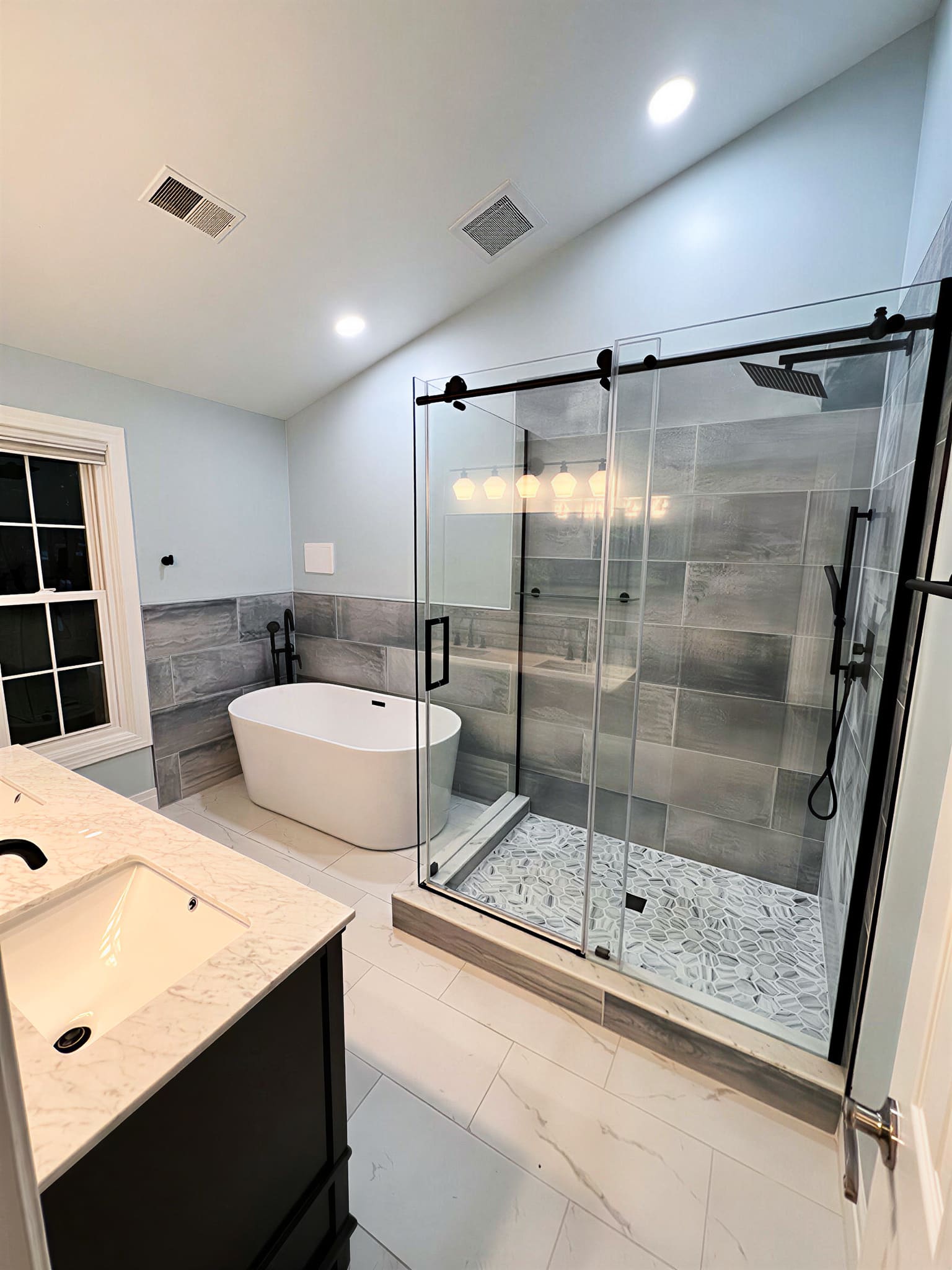 Gray tile walk-in glass shower with freestanding soaking tub