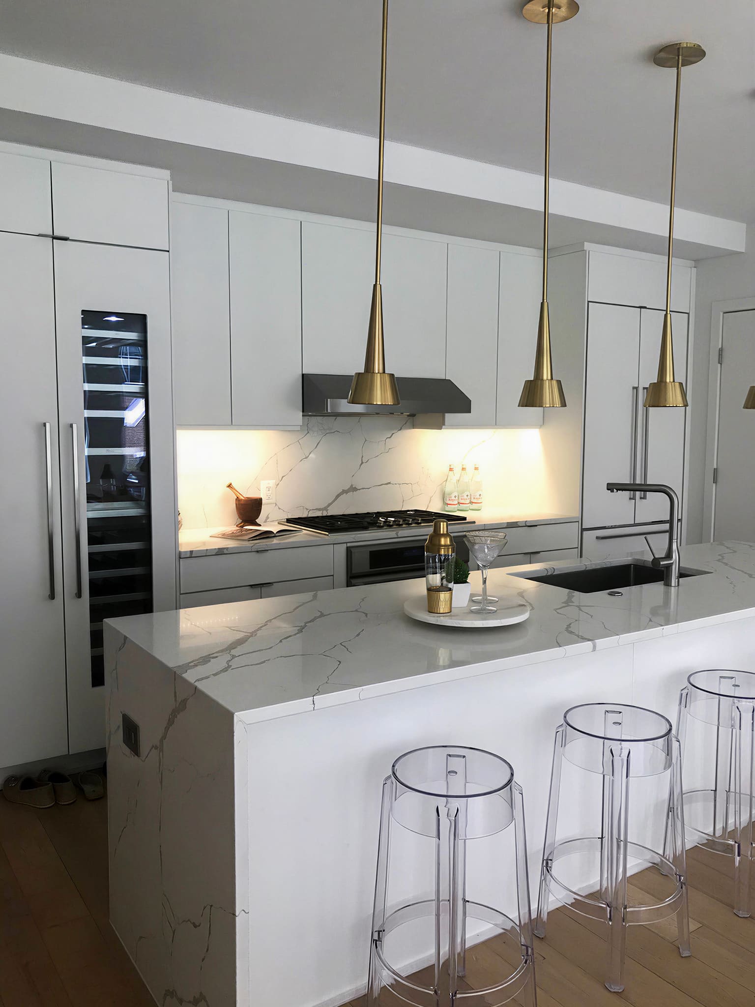 White marble kitchen island with brass pendant lights and wine fridge