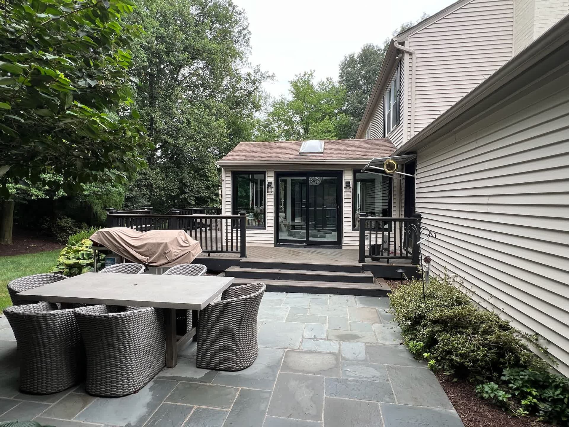 Glass sunroom addition viewed from the stone patio with outdoor dining table