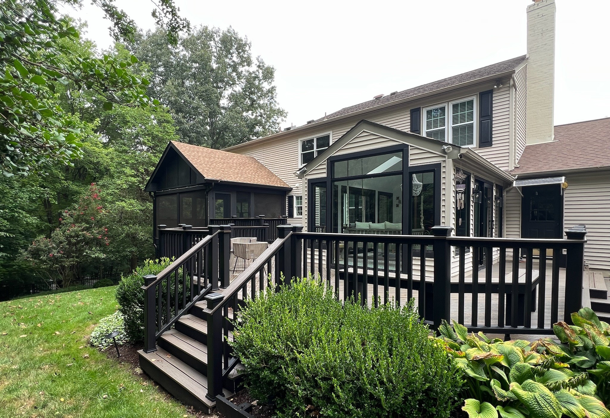 Two-story home exterior with custom black-railed deck, screened porch, and glass sunroom addition