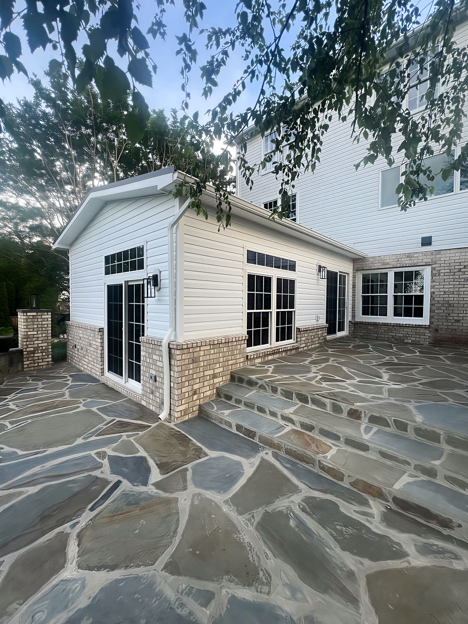 Stone patio with white sunroom addition and brick foundation