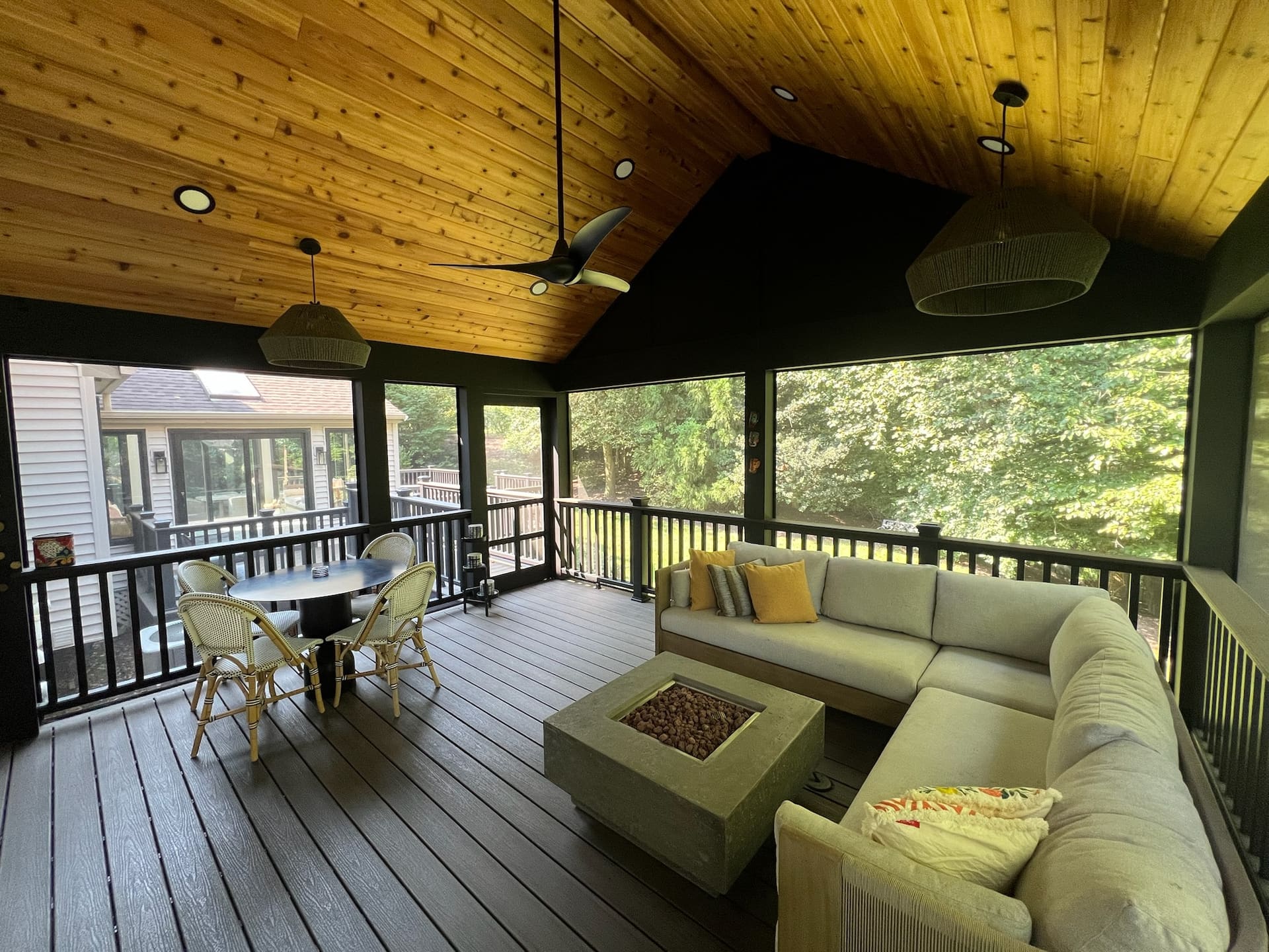 Vaulted screened-in porch with sectional seating, dining area, ceiling fan and fire pit table